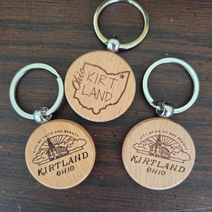 Four wooden keychains with metal rings on a dark wooden surface