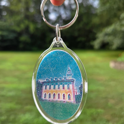 Keychain with a building design on a blue background held against a green leafy background